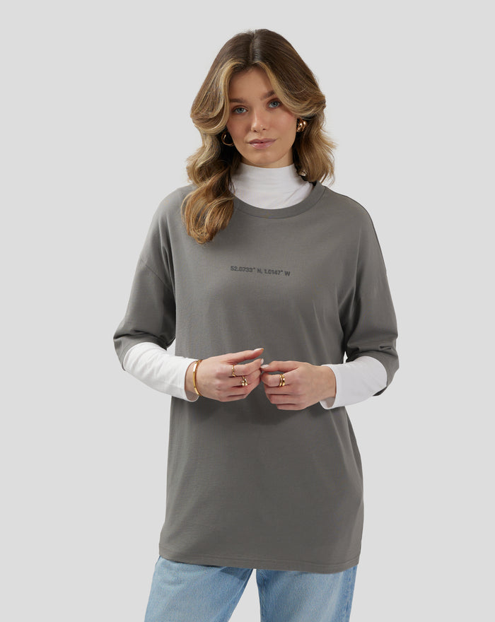 Full body view of a model in a charcoal grey oversized T shirt paired with jeans and sneakers.