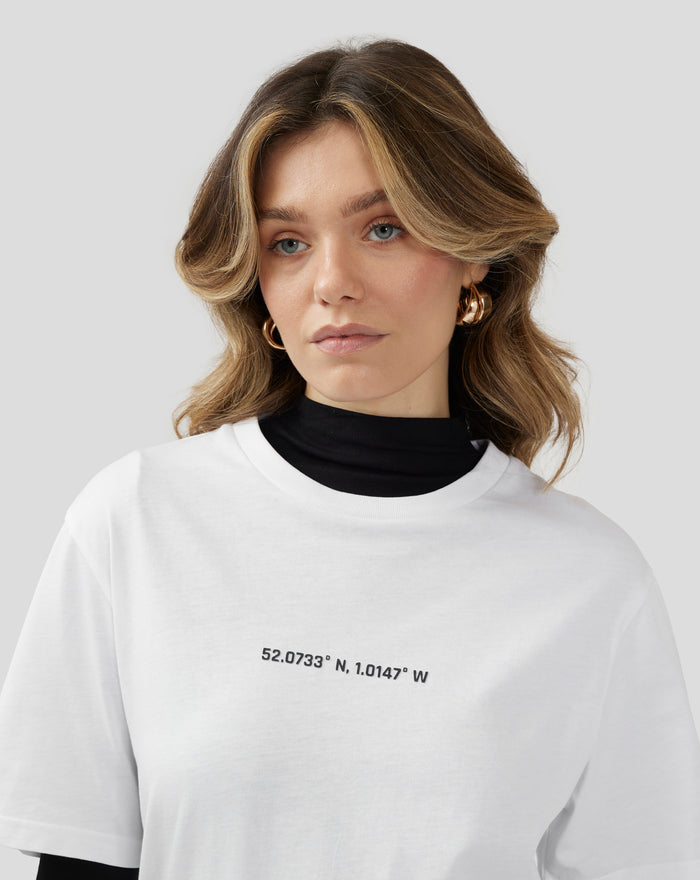 Portrait of a woman wearing a white Silverstone Core Graphic T Shirt over a black turtleneck with coordinates printed on the chest