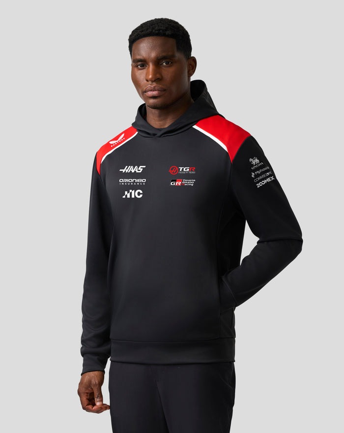 Male model wearing Official Haas Team Unisex Pullover Hoodie in black with red shoulders and chest logos.